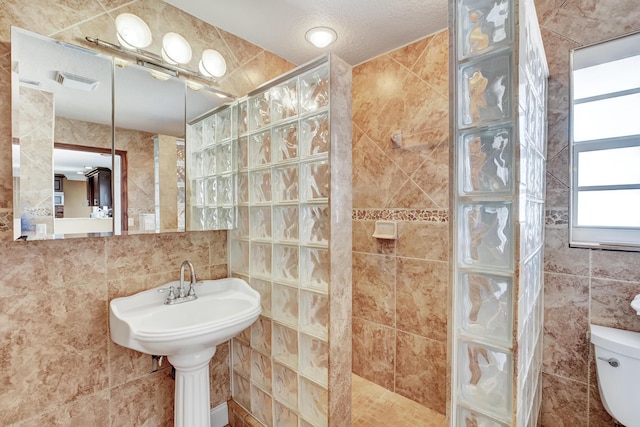 bathroom with tile walls, toilet, a textured ceiling, and walk in shower