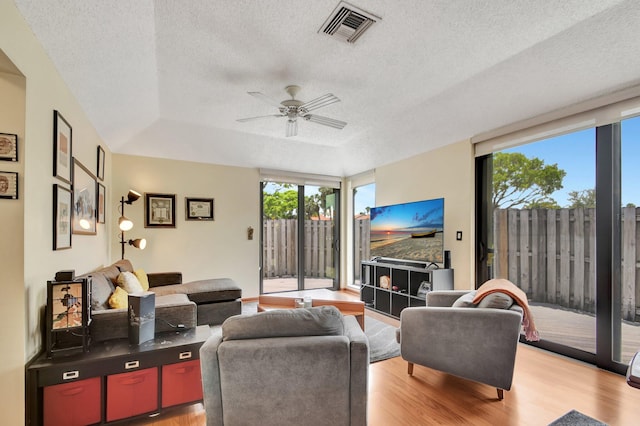 living room with a tray ceiling, ceiling fan, light hardwood / wood-style floors, and a textured ceiling