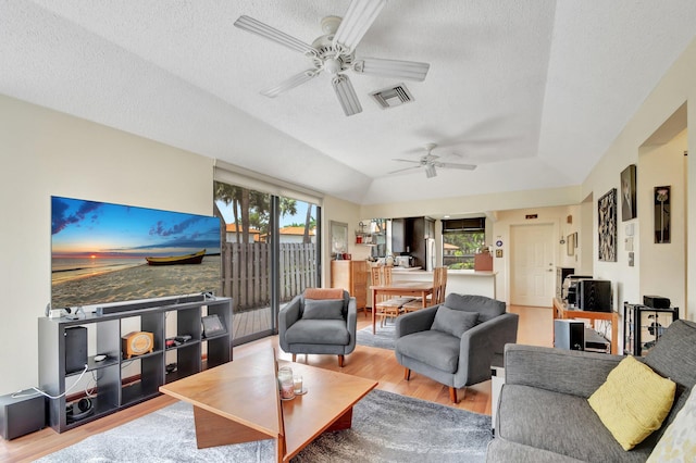 living room featuring a textured ceiling, light hardwood / wood-style floors, vaulted ceiling, and ceiling fan