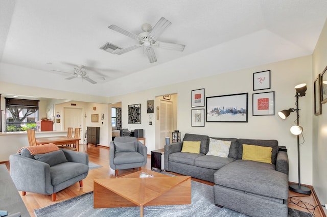 living room with light hardwood / wood-style floors, a raised ceiling, and ceiling fan