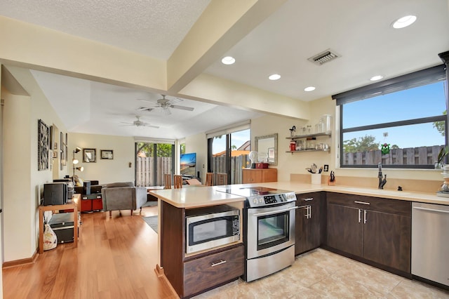 kitchen featuring sink, beamed ceiling, dark brown cabinets, kitchen peninsula, and stainless steel appliances