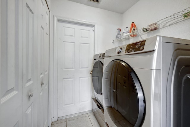 clothes washing area with washer and dryer and light tile patterned floors