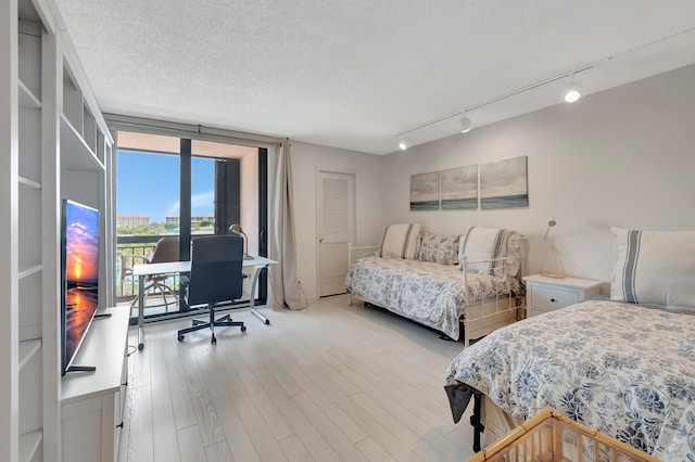 bedroom featuring a closet, light hardwood / wood-style flooring, a textured ceiling, and track lighting