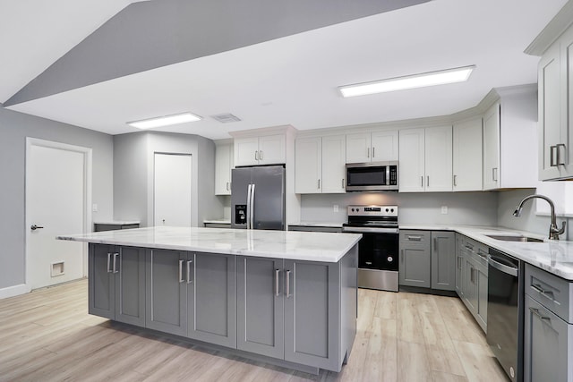 kitchen with light hardwood / wood-style flooring, a kitchen island, stainless steel appliances, gray cabinetry, and sink