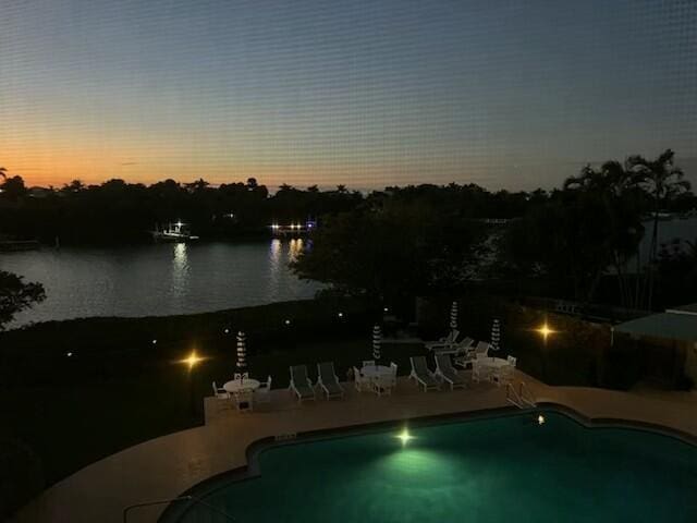 pool at dusk featuring a patio, a water view, and a water slide