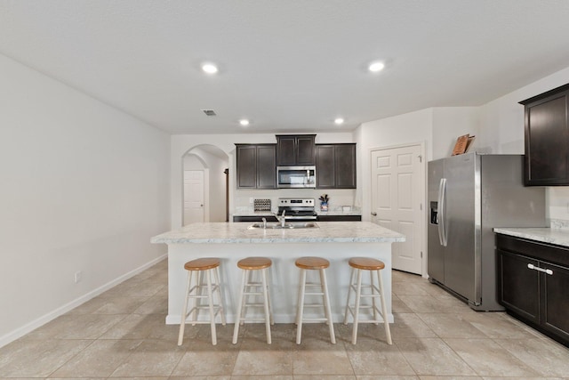 kitchen with dark brown cabinets, stainless steel appliances, a center island with sink, and a breakfast bar area