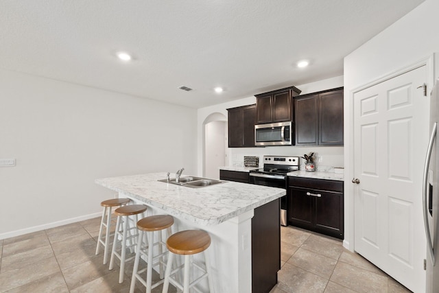 kitchen featuring sink, dark brown cabinets, stainless steel appliances, a breakfast bar area, and a kitchen island with sink