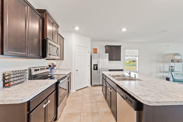 kitchen featuring appliances with stainless steel finishes, sink, an island with sink, dark brown cabinets, and light tile patterned floors