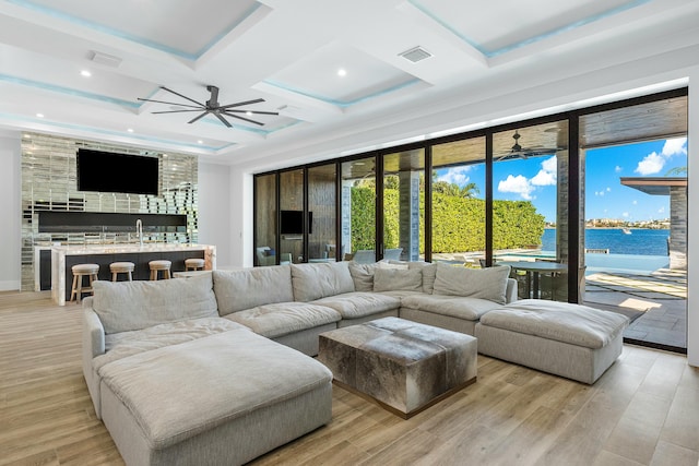 bar featuring light stone countertops, a raised ceiling, ceiling fan, sink, and light hardwood / wood-style floors