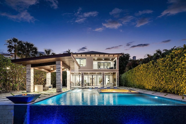 pool at dusk featuring an in ground hot tub and a water view