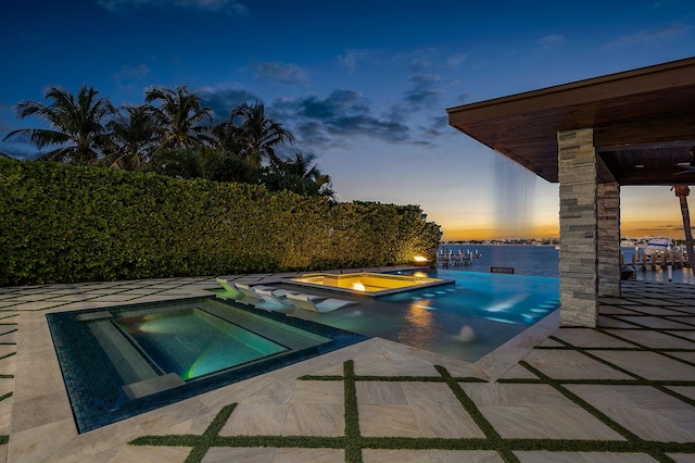 pool at dusk featuring an in ground hot tub and a water view