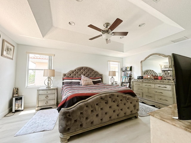 bedroom featuring light hardwood / wood-style flooring, ceiling fan, a textured ceiling, and a raised ceiling