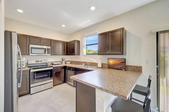 kitchen featuring kitchen peninsula, dark brown cabinets, stainless steel appliances, sink, and a breakfast bar area