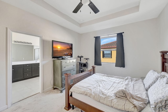 bedroom with a raised ceiling, connected bathroom, ceiling fan, and light carpet