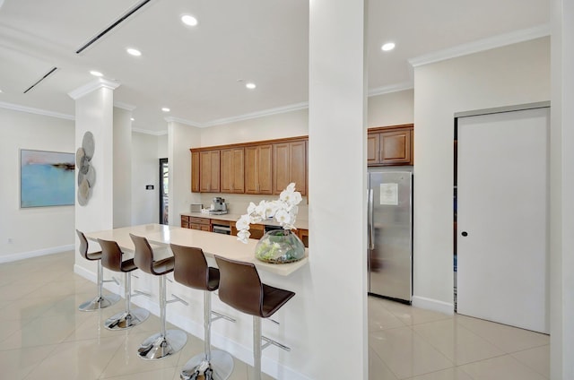 kitchen featuring crown molding, stainless steel refrigerator, a breakfast bar area, and light tile patterned flooring