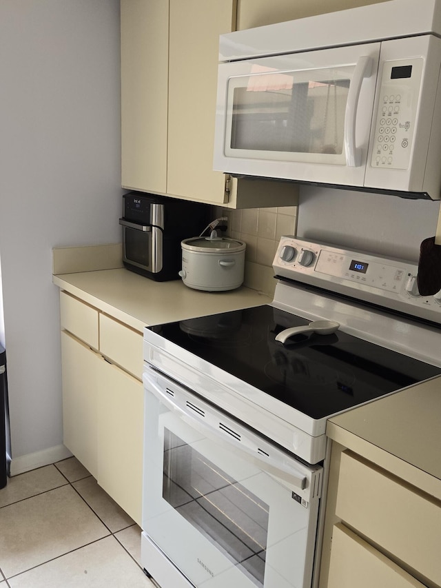 kitchen featuring cream cabinets, white appliances, and light tile patterned floors