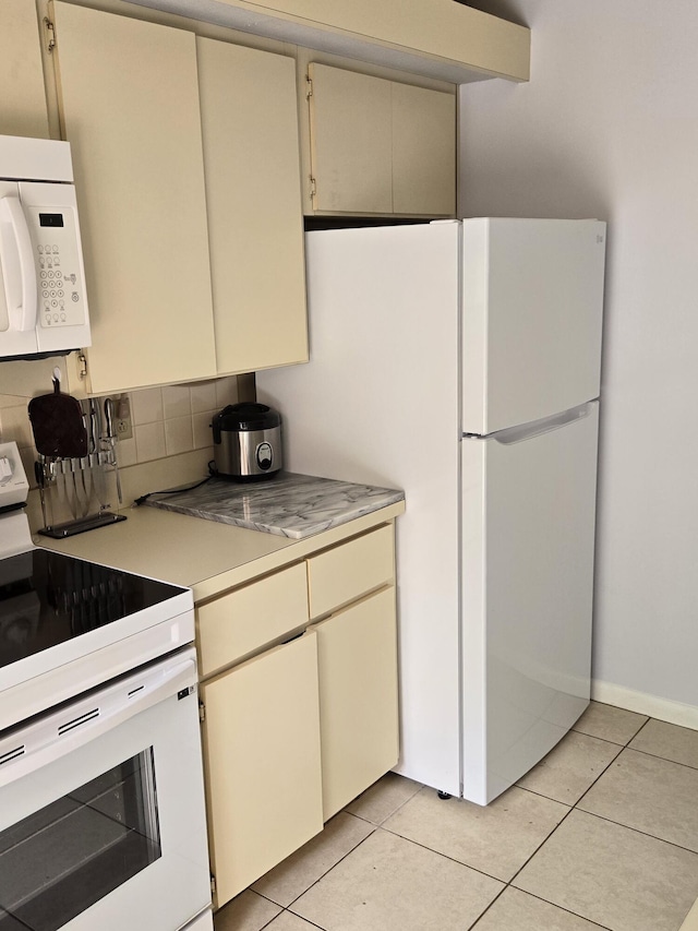 kitchen featuring cream cabinetry, white appliances, light tile patterned floors, and decorative backsplash