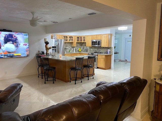 bar featuring backsplash, ceiling fan, light stone countertops, light tile patterned flooring, and stainless steel appliances