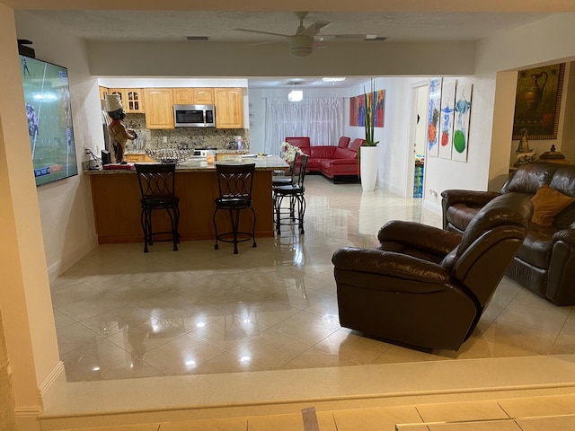 kitchen with kitchen peninsula, a kitchen breakfast bar, backsplash, ceiling fan, and light tile patterned floors