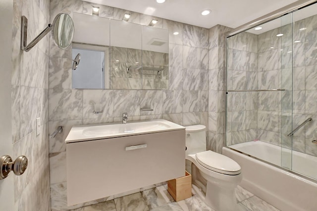 full bathroom with vanity, toilet, bath / shower combo with glass door, and tile walls