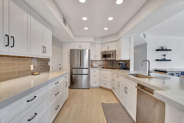 kitchen featuring appliances with stainless steel finishes, light wood-type flooring, tasteful backsplash, sink, and white cabinets