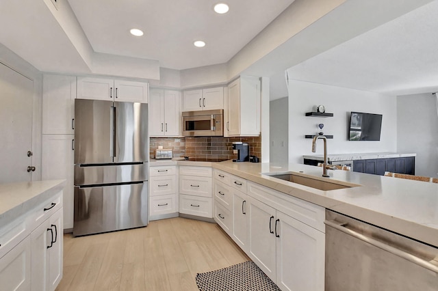 kitchen with sink, stainless steel appliances, tasteful backsplash, light hardwood / wood-style floors, and white cabinets