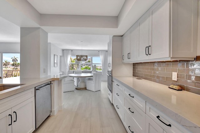 kitchen with pendant lighting, stainless steel appliances, white cabinetry, and light hardwood / wood-style flooring