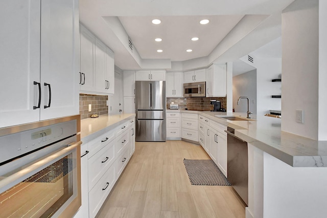 kitchen featuring white cabinets, sink, light hardwood / wood-style flooring, kitchen peninsula, and stainless steel appliances