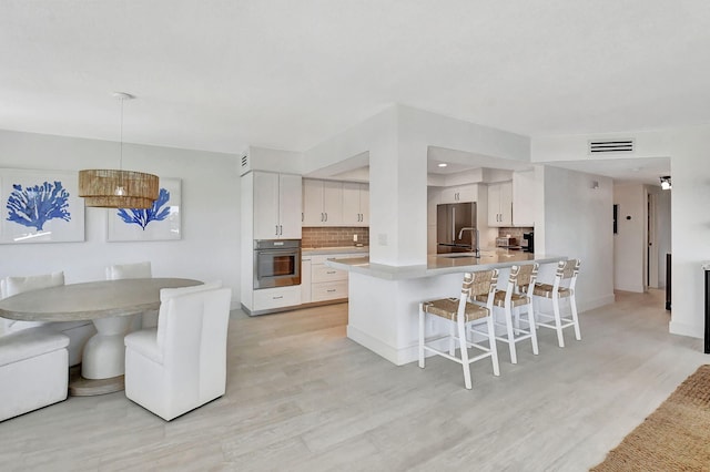 kitchen featuring backsplash, white cabinets, light hardwood / wood-style flooring, decorative light fixtures, and stainless steel appliances