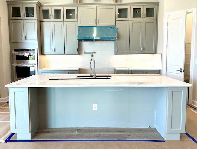 kitchen with decorative backsplash, light stone countertops, stainless steel double oven, and ventilation hood