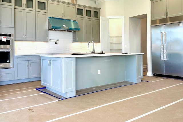 kitchen with a kitchen island with sink, sink, appliances with stainless steel finishes, and tasteful backsplash