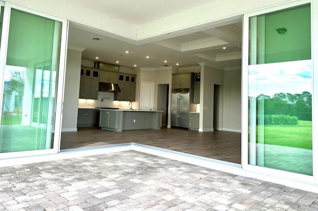 interior space with tasteful backsplash, ornamental molding, open floor plan, stainless steel built in refrigerator, and under cabinet range hood