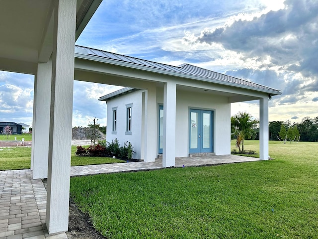 exterior space featuring french doors, metal roof, a standing seam roof, a yard, and stucco siding