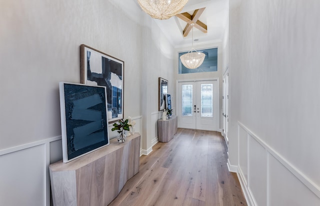 entrance foyer with french doors, a decorative wall, light wood-style flooring, an inviting chandelier, and ornamental molding