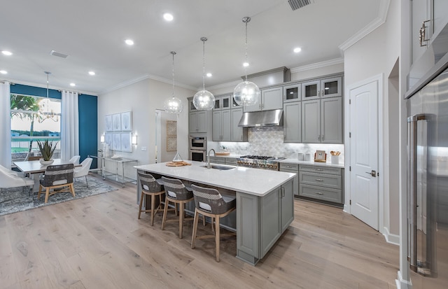 kitchen featuring decorative backsplash, decorative light fixtures, a center island with sink, and light hardwood / wood-style floors