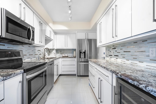 kitchen featuring appliances with stainless steel finishes, track lighting, decorative backsplash, stone countertops, and beverage cooler