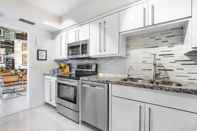 kitchen with appliances with stainless steel finishes, dark stone countertops, sink, backsplash, and light tile patterned flooring