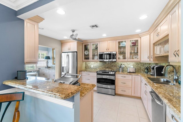 kitchen with kitchen peninsula, sink, light brown cabinetry, appliances with stainless steel finishes, and tasteful backsplash