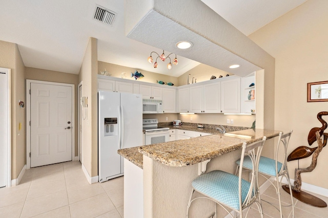 kitchen featuring vaulted ceiling, kitchen peninsula, white appliances, and a breakfast bar