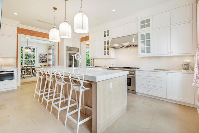 kitchen featuring pendant lighting, high end appliances, a kitchen island with sink, white cabinetry, and extractor fan