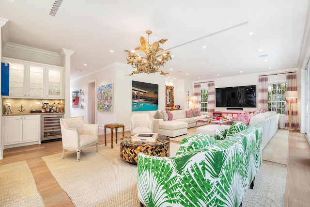 living room with beverage cooler, an inviting chandelier, light hardwood / wood-style flooring, bar, and ornamental molding