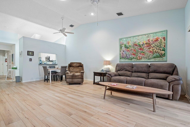 living room with light wood-type flooring, a textured ceiling, vaulted ceiling, and ceiling fan