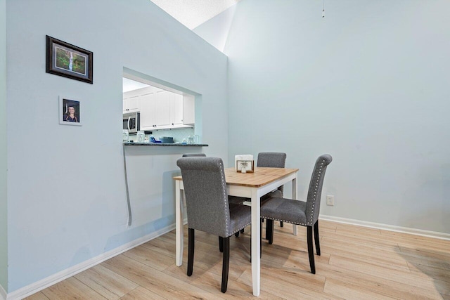 dining space with high vaulted ceiling and light wood-type flooring