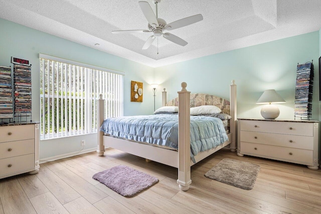 bedroom with light hardwood / wood-style floors, ceiling fan, a raised ceiling, and a textured ceiling