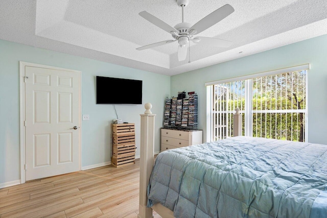 bedroom with a textured ceiling, a raised ceiling, ceiling fan, and light hardwood / wood-style flooring