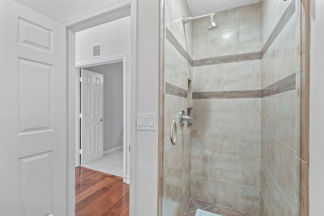 bathroom with a tile shower and wood-type flooring