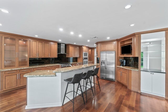 kitchen with wall chimney exhaust hood, dark hardwood / wood-style floors, a kitchen island, and appliances with stainless steel finishes