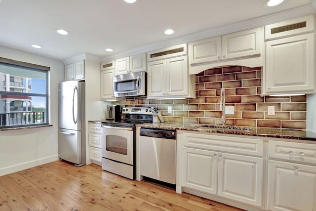 kitchen with decorative backsplash, appliances with stainless steel finishes, dark stone counters, light hardwood / wood-style floors, and white cabinetry