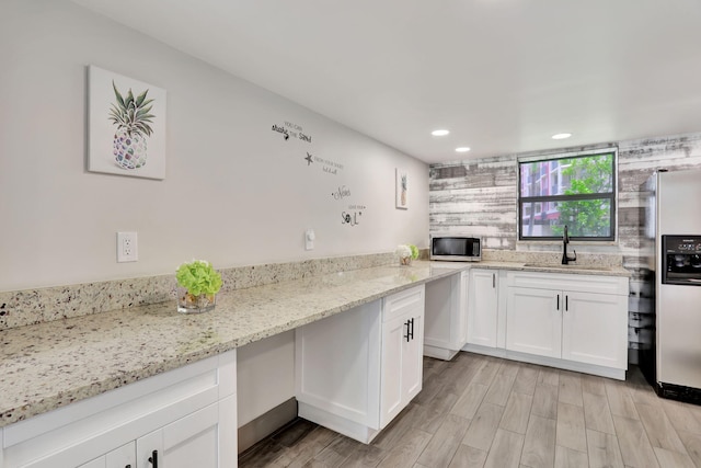 kitchen with sink, light stone countertops, light hardwood / wood-style floors, white cabinetry, and stainless steel appliances