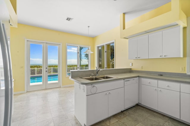 kitchen featuring visible vents, a peninsula, stainless steel refrigerator, a sink, and dishwasher